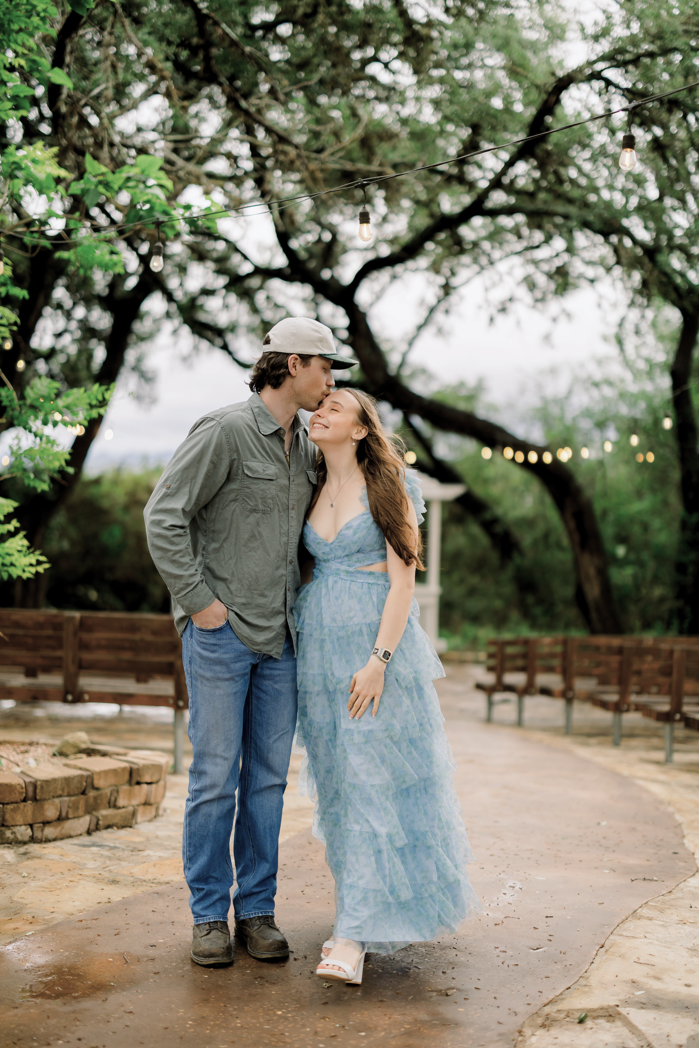 A kiss under the string lights by the benches