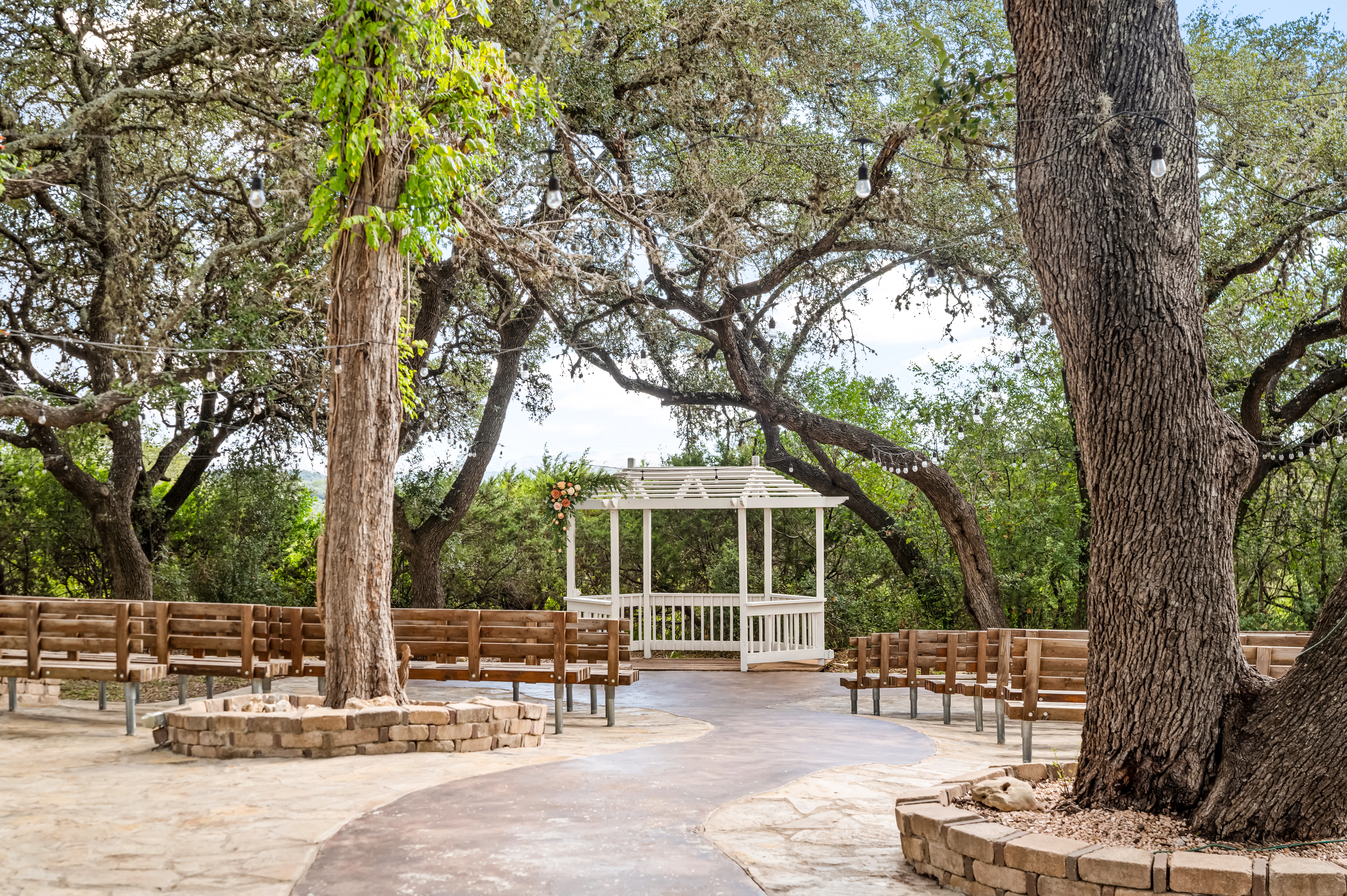 The ceremony gazebo under the oaks, with wooden benches and string lights