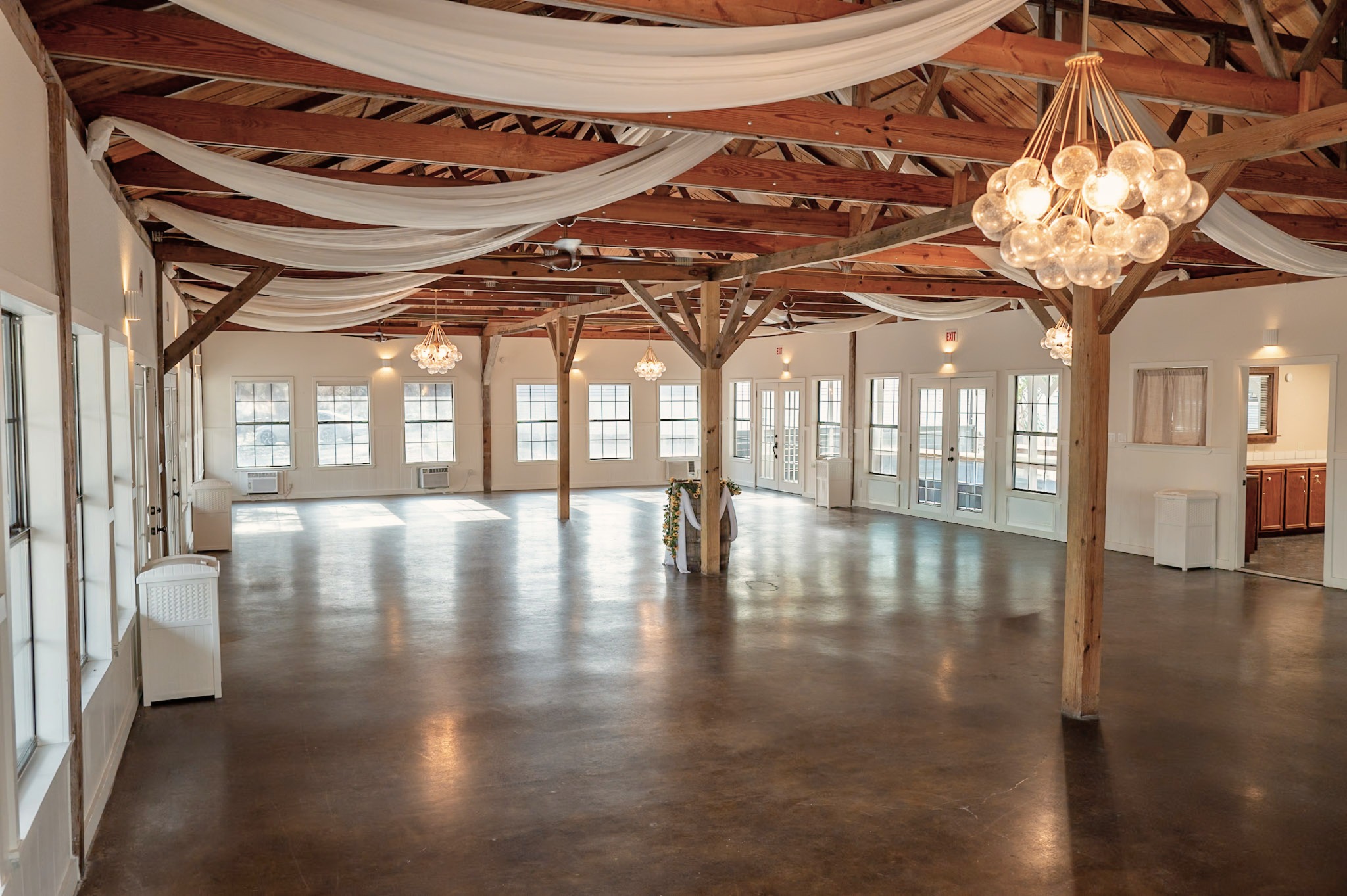 Inside the hall: open floor, timber trusses, ceiling draping and bubble chandeliers