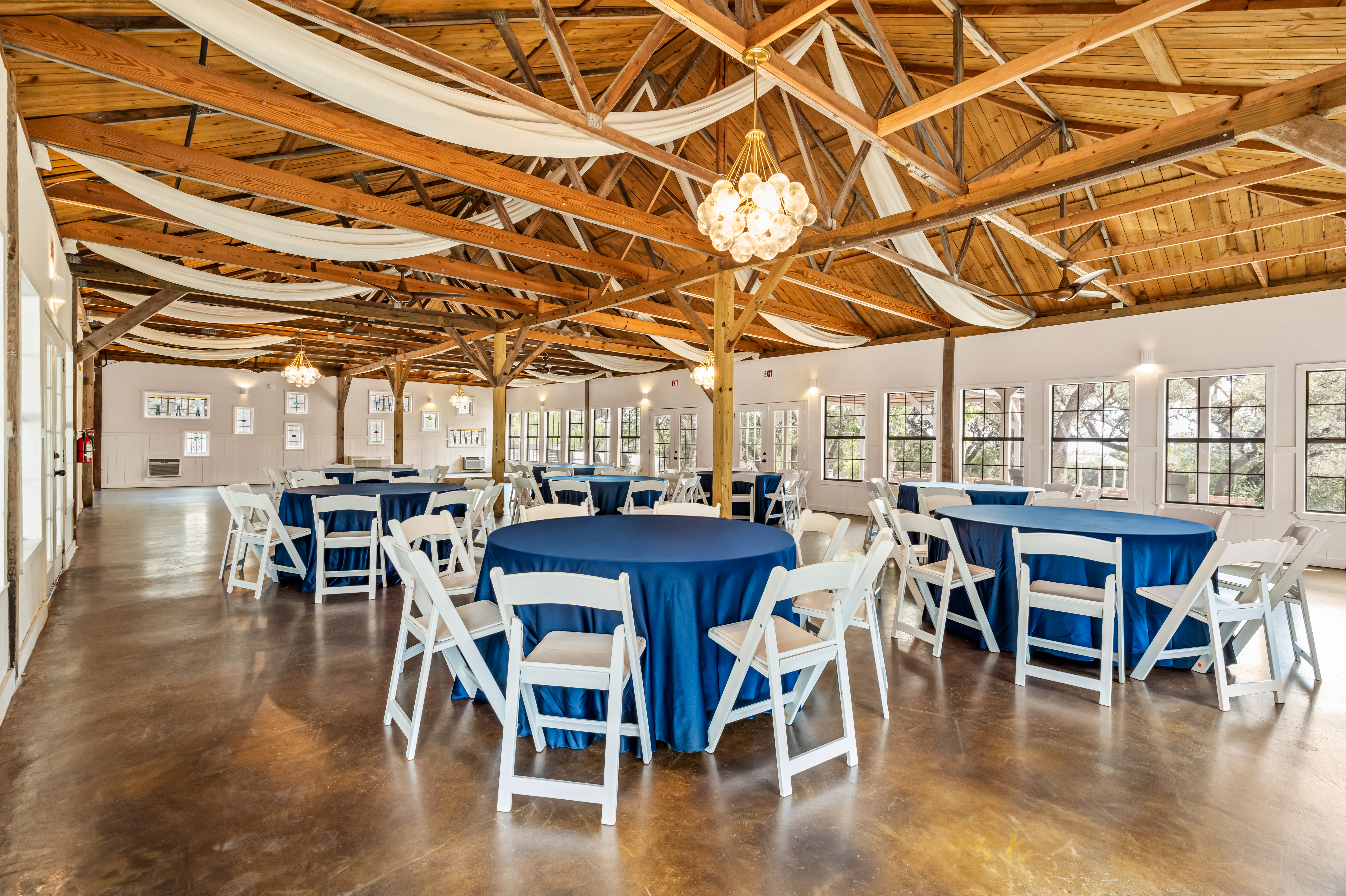 Round tables in blue linens under timber trusses and bubble chandeliers