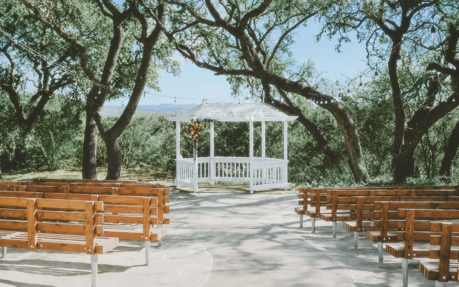 The white lakeside gazebo strung with lights, benches set for a ceremony